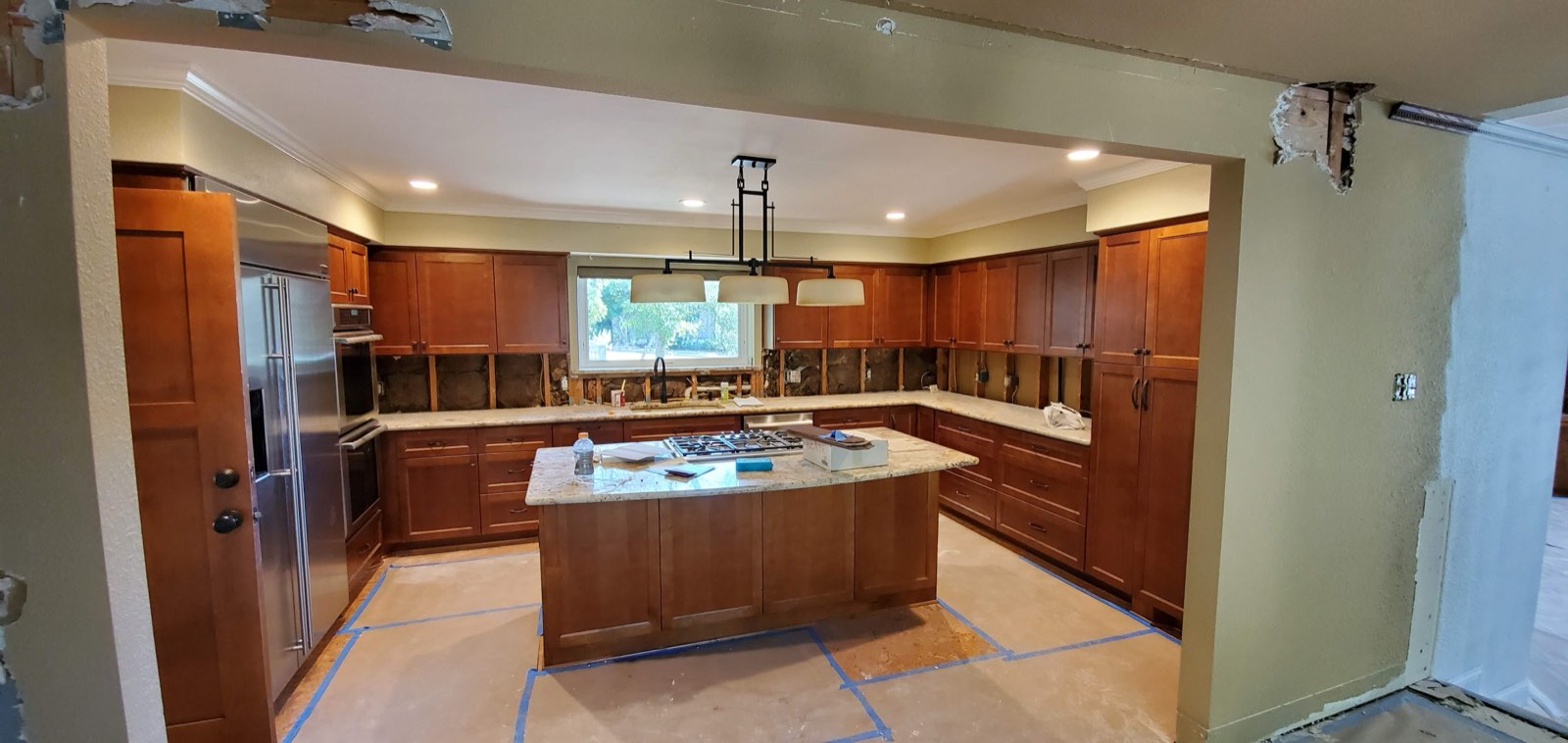 Kitchen before painting: dark cherry wood cabinets, granite island, bare patched walls