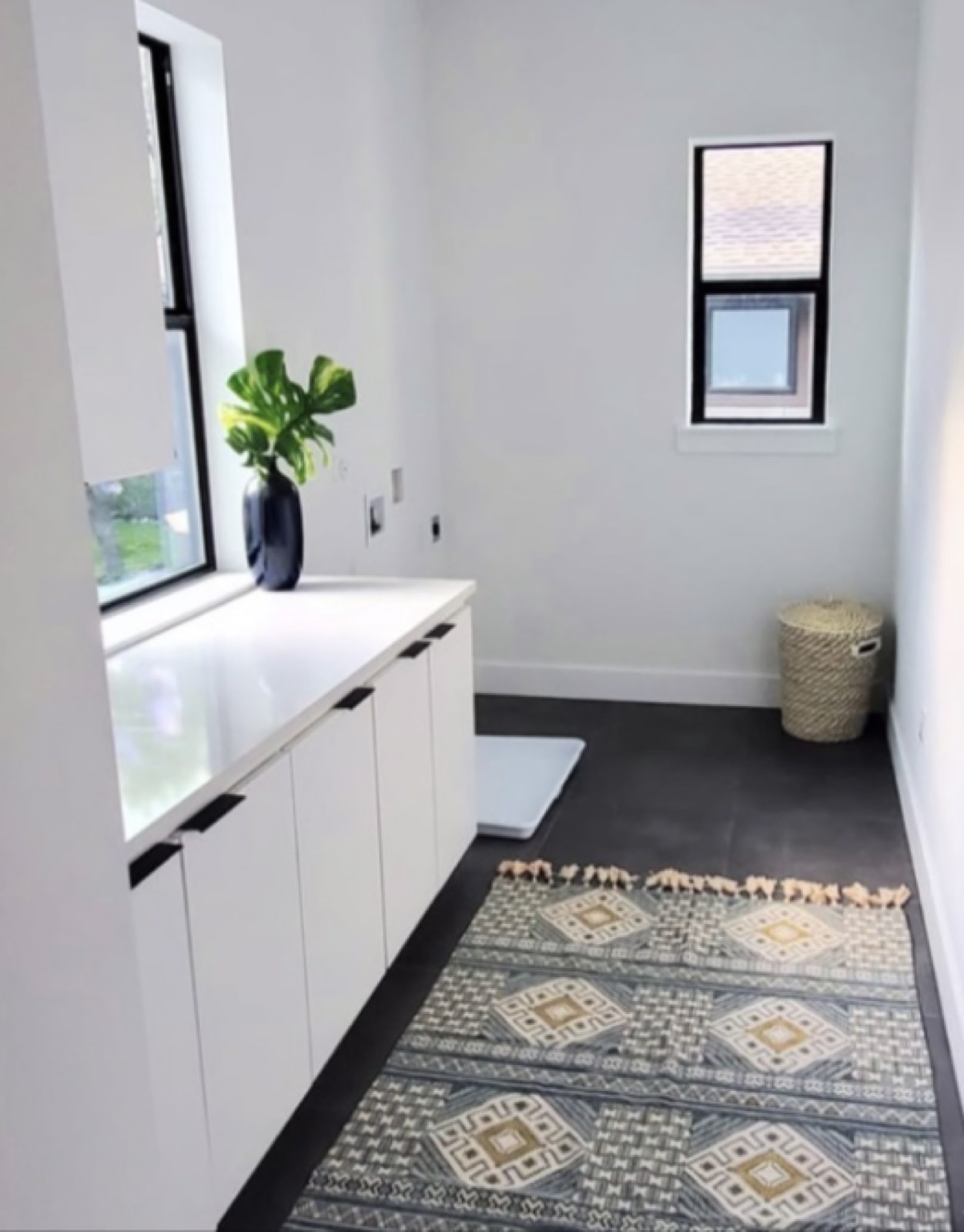 Narrow utility room with white cabinets, white walls and a black framed window